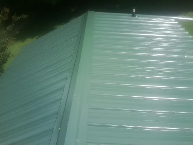 New green metal panels meeting at the ridge of a roof — Flat Roof Repair work by our crew in Fargo