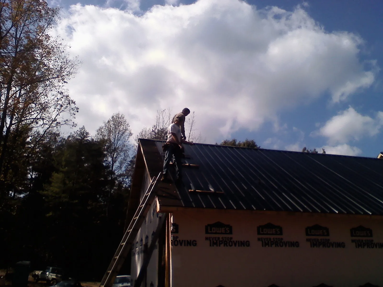Roofer fastening dark metal panels high against a cloudy sky, from a Roof Inspection job in Fargo