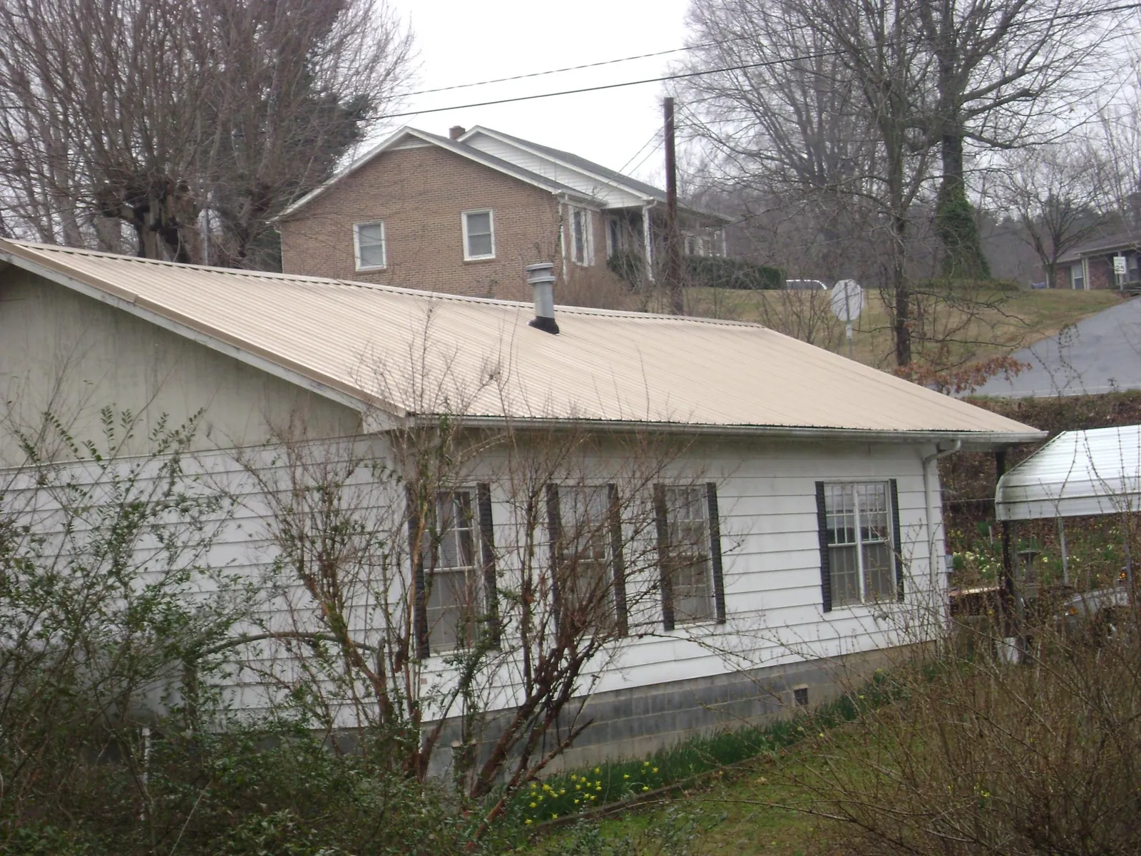 Tan metal roof on a white sided house set into a hillside — Commercial Roofing by Roofing Brothers in Fargo